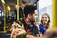 Woman and boy having a conversation, smiling, sitting in a bus. Other people in the background.