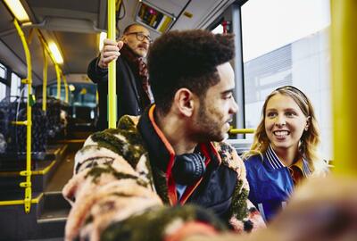 Woman and boy having a conversation, smiling, sitting in a bus. Other people in the background.